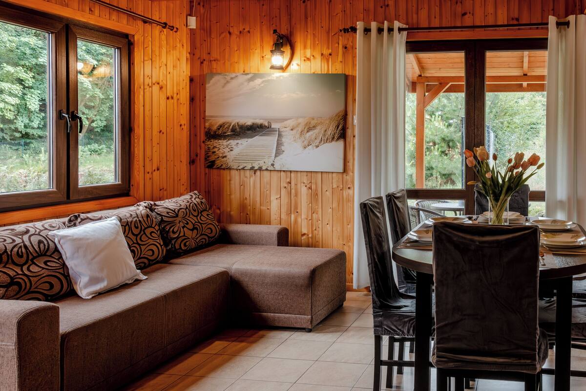 A wooden interior with a sofa, dining table, chairs, and a painting of a landscape.