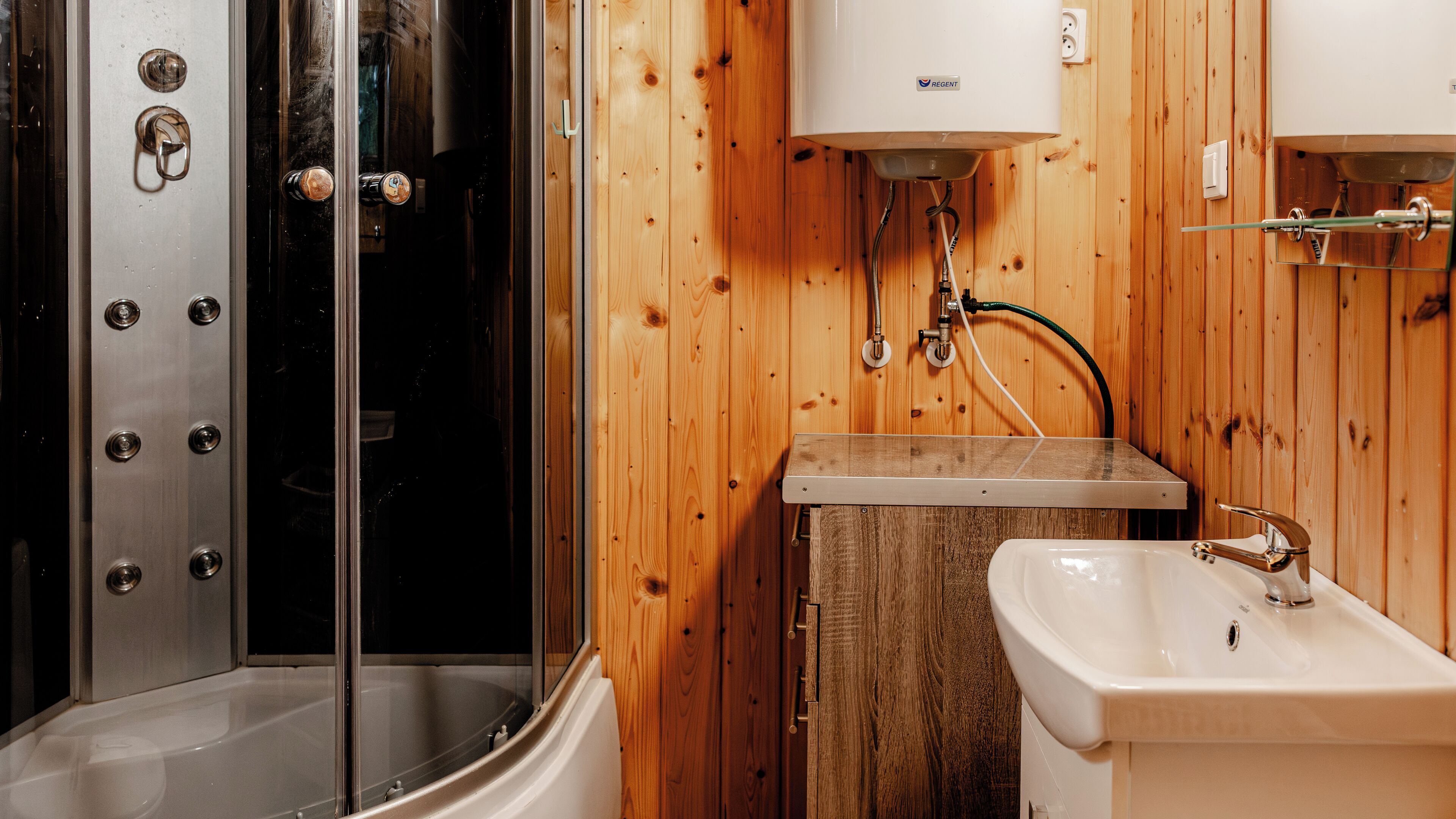 A bathroom with a glass-enclosed shower, a white sink, and a wooden wall.