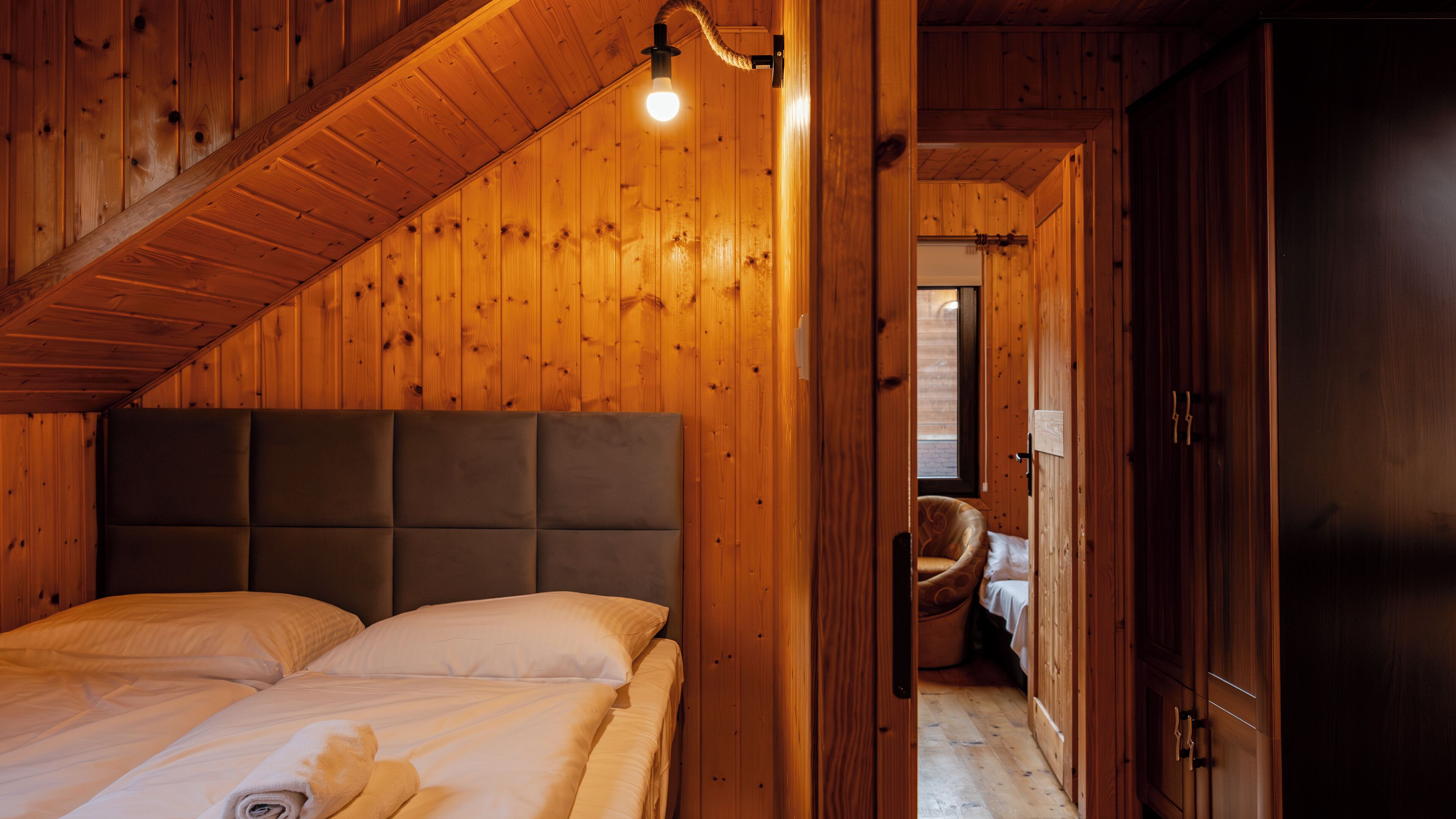 Een slaapkamer in een houten hutje, met een bed, een stoel en een kledingkast.