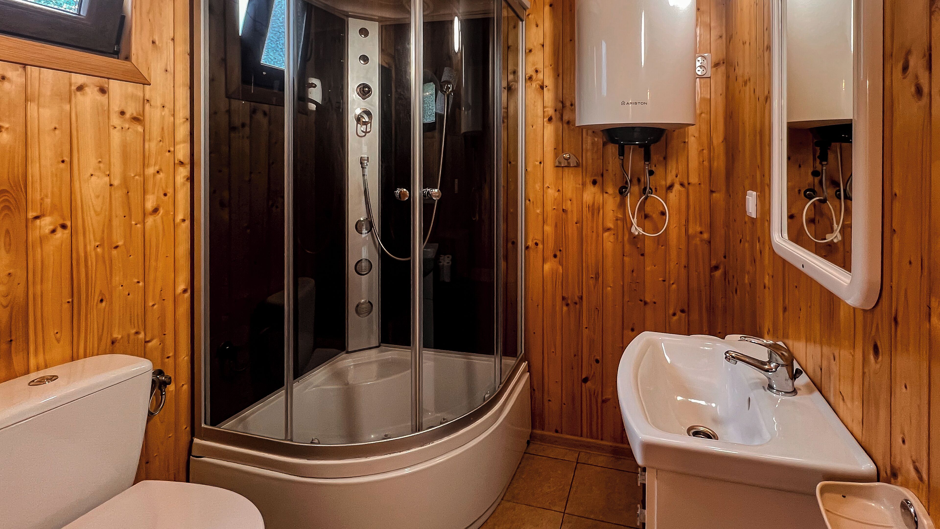 Ein Badezimmer einer Holz-Blockhütte mit einer gläsernen Duschkabine, einer Toilette und einem Waschbecken.