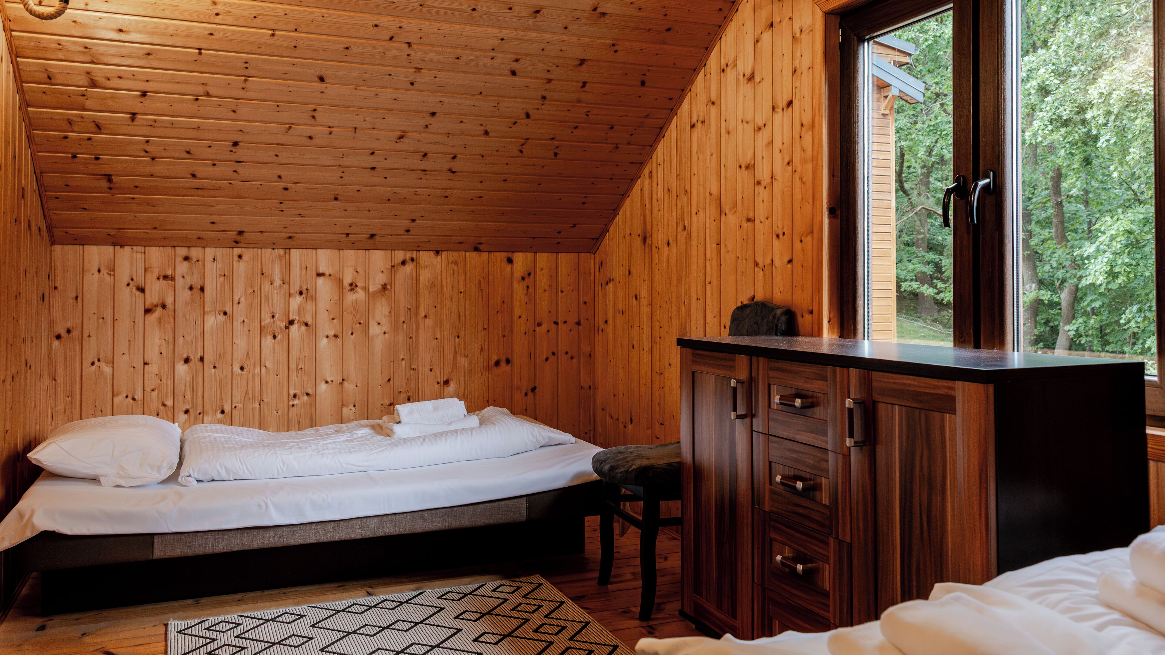 Une chambre dans une cabane en bois, avec un lit, une commode et une fenêtre donnant sur un paysage verdoyant.