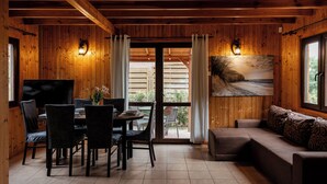 Een houten interieur met een eethoek, een bank en een groot raam met uitzicht op het strand.