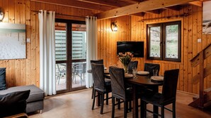 Een houten interieur met een eethoek, een bank en een aan de muur bevestigde televisie.