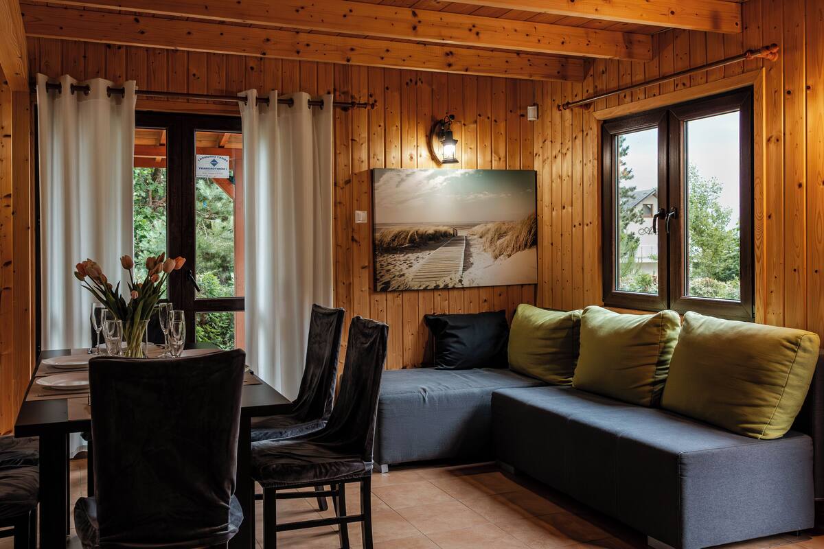 A cozy cabin interior with a dining area, a sofa with cushions, and a painting on the wall.
