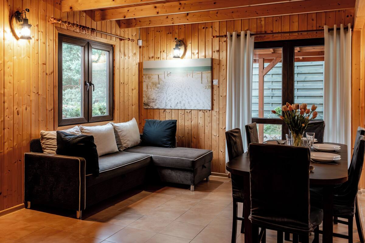 A cozy cabin interior with a wooden interior, a sofa, a dining table with chairs, and a painting on the wall.