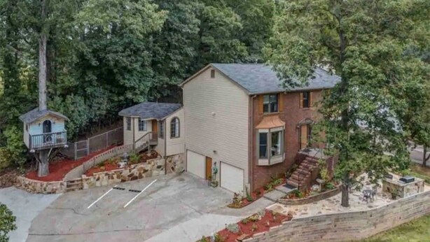 A two-story building with a small attached structure, a driveway, and a landscaped area with a stone wall and red mulch. - estudio proyector (Marietta)