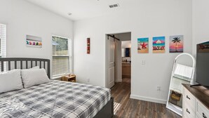 Ein Schlafzimmer mit einem Bett, einer Kommode, einem Spiegel und einer Tür zu einem Badezimmer.