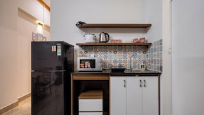 A compact kitchen with a black refrigerator, a microwave, a wooden countertop, and a tiled backsplash. - Hearth and Home De Tham (Ho Chi Minh City)