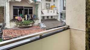A balcony with a tiled floor, a white wall, and a view of a building with a balcony and clothes hanging outside. - Hearth and Home De Tham (Ho Chi Minh City)