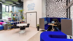Un ufficio moderno con posti a sedere blu e grigi, un tavolo bianco e una persona che lavora alla scrivania.