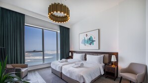 Habitación de hotel moderna con una cama grande, dos mesitas de noche, vista al mar y un amplio ventanal con cortinas.