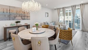 Et moderne spiseområde med et rundt bord, stole, en lysekrone og udsigt over byen gennem store vinduer.