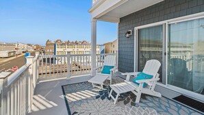 En balkon med hvide Adirondack-stole og et mønstret tæppe.