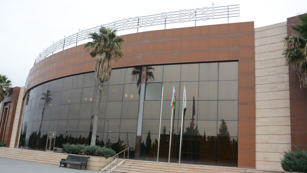 A modern building with a curved facade, large glass windows, and a palm tree in front. - Arena Hotel Imishli (Imishli)