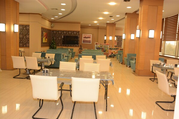 A spacious dining area with multiple tables and chairs, a Christmas tree, and a television screen on the wall.