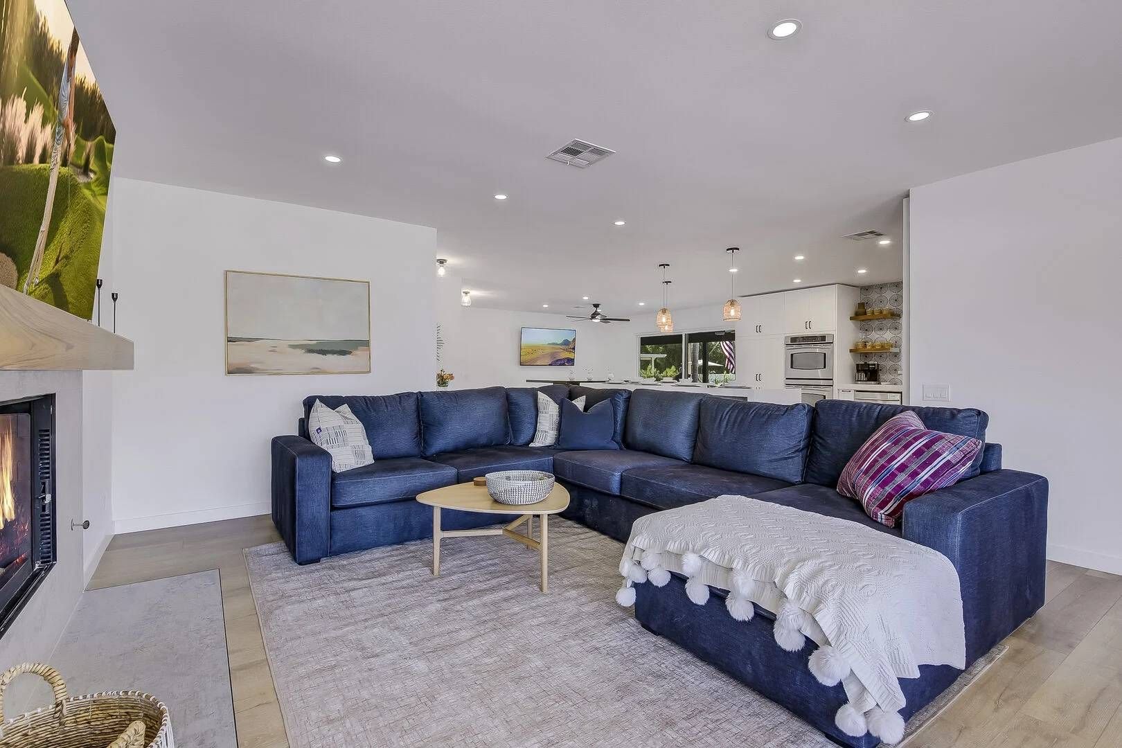 A modern living room with a sectional sofa, a fireplace, and a kitchen in the background.