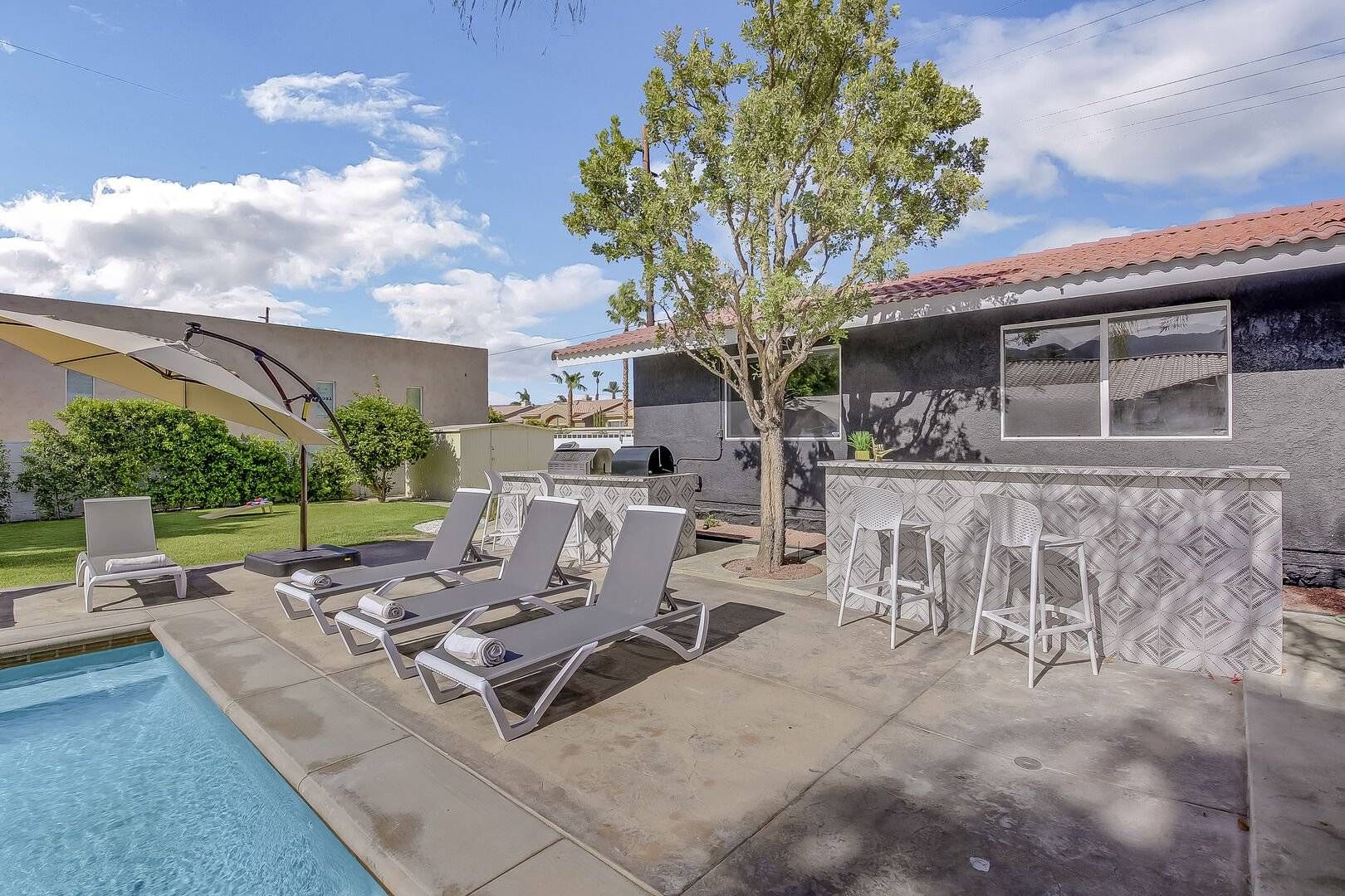 A poolside area with lounge chairs, a barbecue grill, and a bar with patterned tiles.