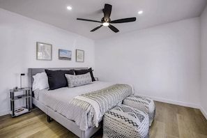 A bedroom with a bed, bedside tables, a ceiling fan, and framed pictures on the wall.