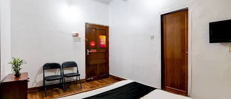 A hotel room with a bed, two chairs, a wooden door, and a television on the wall.