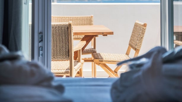 A room with a large window, wicker furniture, and a view of the sea. - Liberty Suites Spetses  (Spetses)