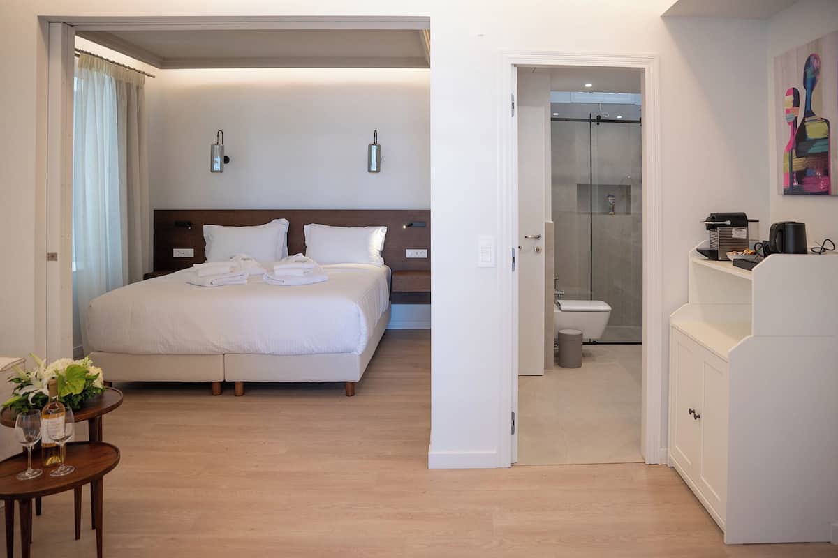 Una habitación de hotel con una cama grande, mesitas de noche, un baño con ducha y una kitchenette.