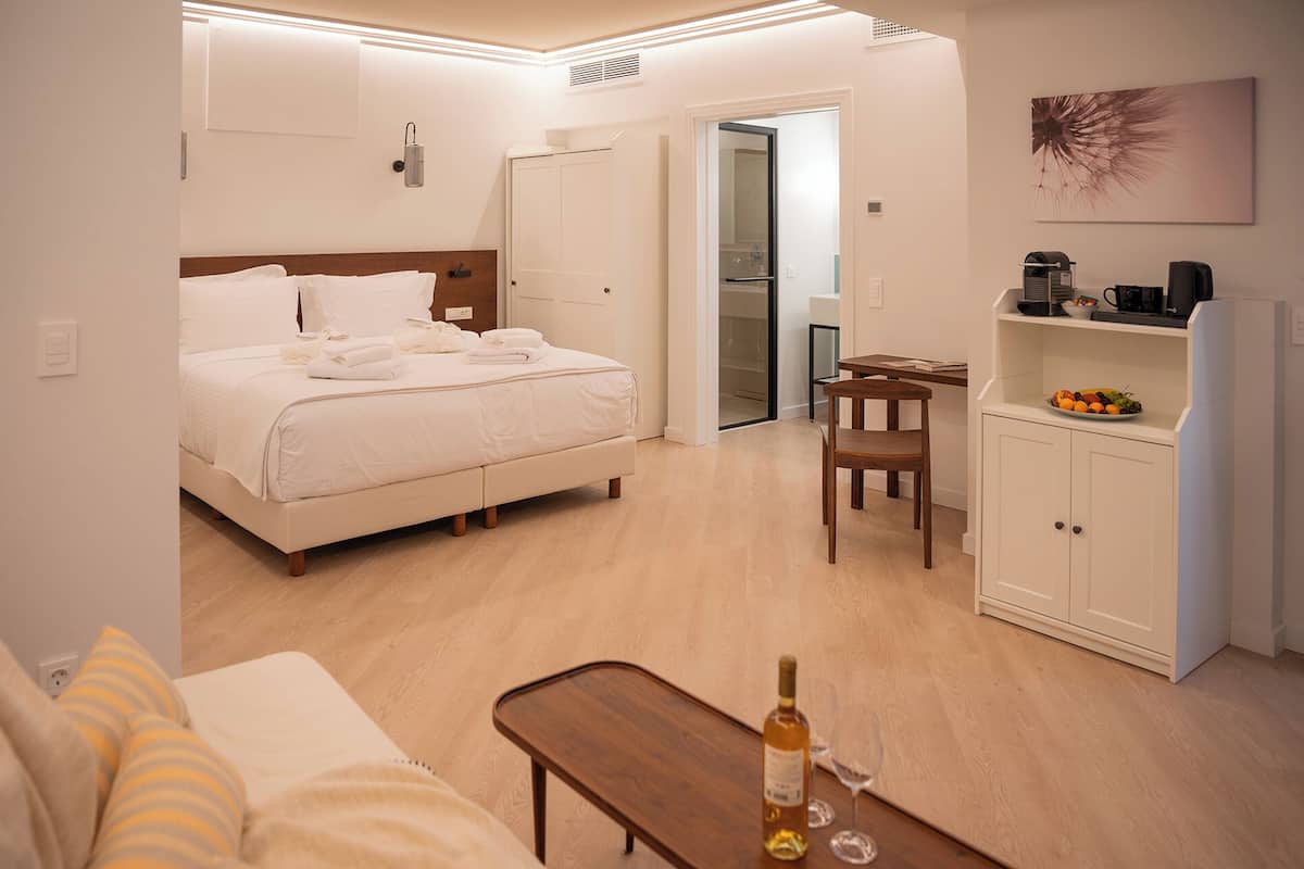 Habitación de hotel con cama, escritorio, silla, una mesita, armario y una botella de vino.
