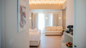 A hotel room with a bed, a sofa, a dining area, and a kitchen counter with fruit. - Liberty Suites Spetses  (Spetses)