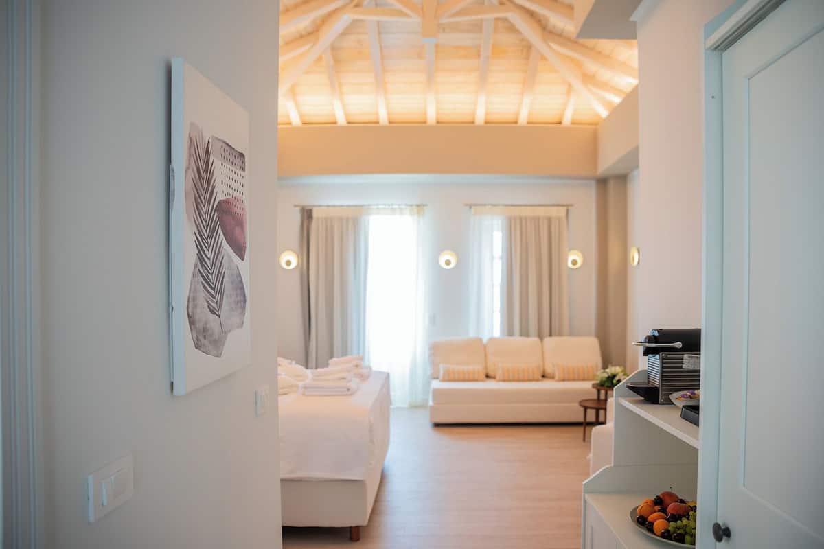 Habitación de hotel con cama, sofá, zona de comedor y encimera de cocina con fruta.