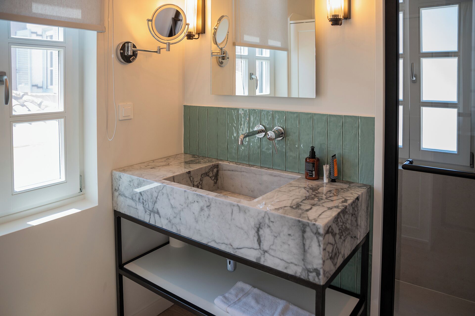 A bathroom with a marble sink, green wall paneling, and two wall-mounted mirrors.
