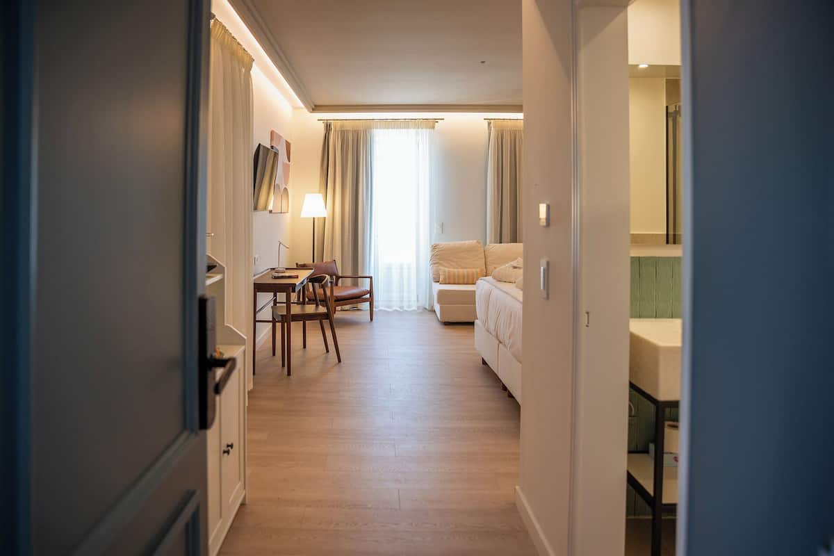 Habitación de hotel con suelo de madera, zona de comedor con mesa y sillas, sofá y cama.