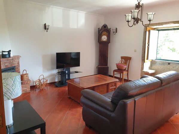 A living room with a leather sofa, a television, a fireplace, and a large wall clock. - Quinta da Vinha Velha · Villa with private pool & views in Minho (Viana do Castelo)