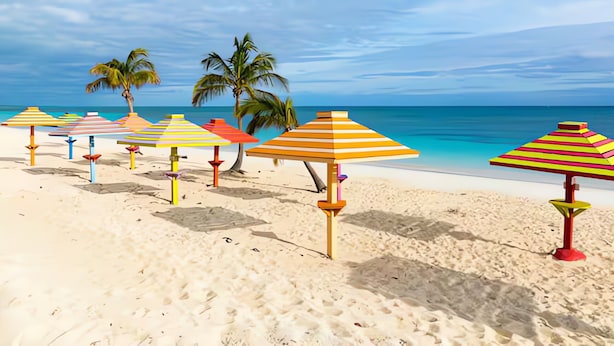 A beach with colorful striped umbrellas and palm trees.