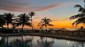 A poolside area with lounge chairs and palm trees during sunset.