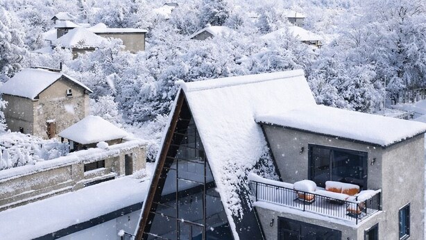 Una casa moderna con fachada de vidrio, piscina y montañas nevadas al fondo.