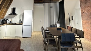 Un loft moderno con vigas de madera a la vista, una cocina con armarios blancos, un comedor con mesa y sillas de madera, y un balcón con barandilla metálica.