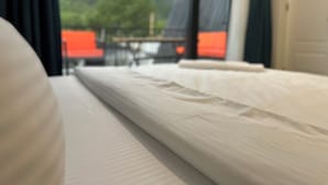 Una cama con colchón blanco y vistas a un balcón con una silla roja y una mesa.
