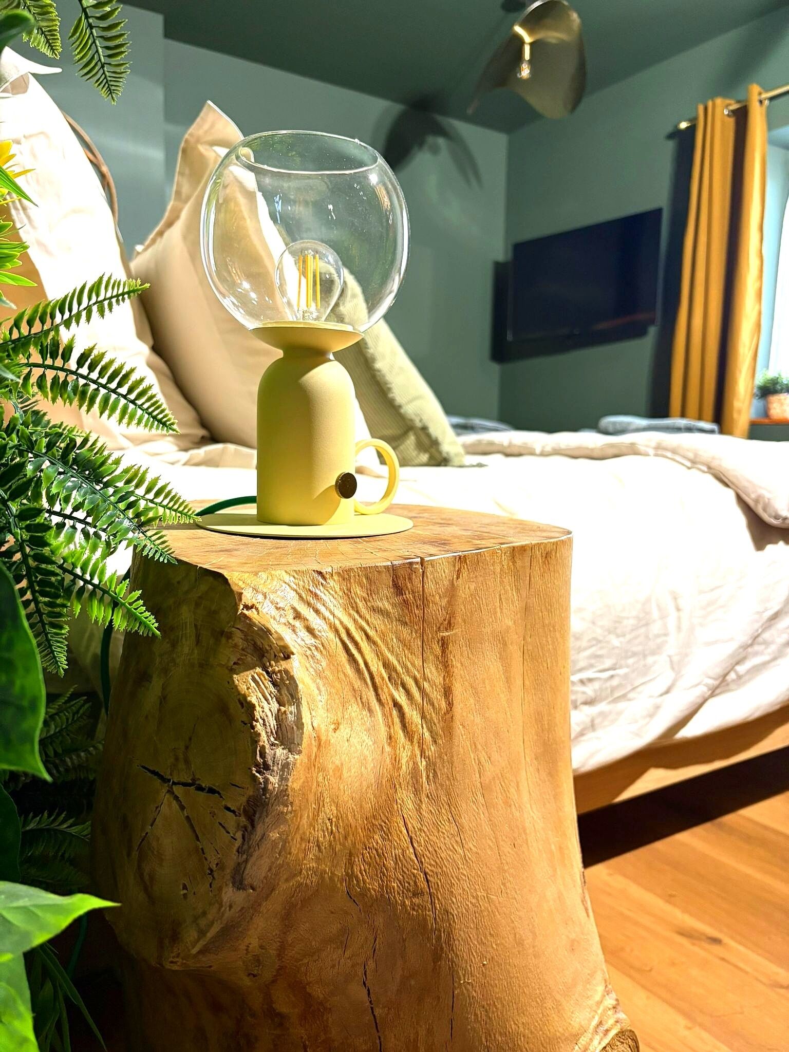 Una cama con cabecera de madera, lámpara de noche y planta en maceta.