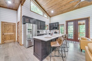 A modern kitchen with a central island, dark cabinets, stainless steel appliances, and a dining area with bar stools. - Creekside Cabin w/ Views & Hot Tub in Broken Bow (Broken Bow)