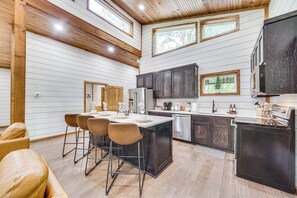 A modern kitchen with a central island, bar stools, and dark cabinetry. - Creekside Cabin w/ Views & Hot Tub in Broken Bow (Broken Bow)