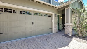 A two-story house with a beige garage door, a brick driveway, and a stone pillar near the entrance. - Tasteful Flagstaff Townhome w/ 2 Furnished Decks (Flagstaff)