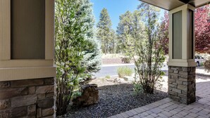 A covered outdoor area with a stone wall, a gravel pathway, and a view of a road with vehicles. - Tasteful Flagstaff Townhome w/ 2 Furnished Decks (Flagstaff)