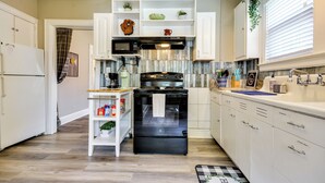 A modern kitchen with white cabinetry, a black stove, and a microwave. There are shelves with plants and kitchen items. - Walk Downtown: Inviting Apartment in Greensboro! (Greensboro)