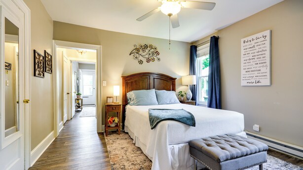 A bedroom with a bed, bedside tables, a ceiling fan, a wall art piece, and a window with curtains. - Walk Downtown: Inviting Apartment in Greensboro! (Greensboro)