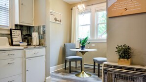 A kitchen with white cabinetry, a chandelier, a dining table with two chairs, and a window with curtains. - Walk Downtown: Inviting Apartment in Greensboro! (Greensboro)