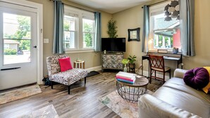 A living room with a sofa, a chair, a coffee table, a TV, and a desk. - Walk Downtown: Inviting Apartment in Greensboro! (Greensboro)