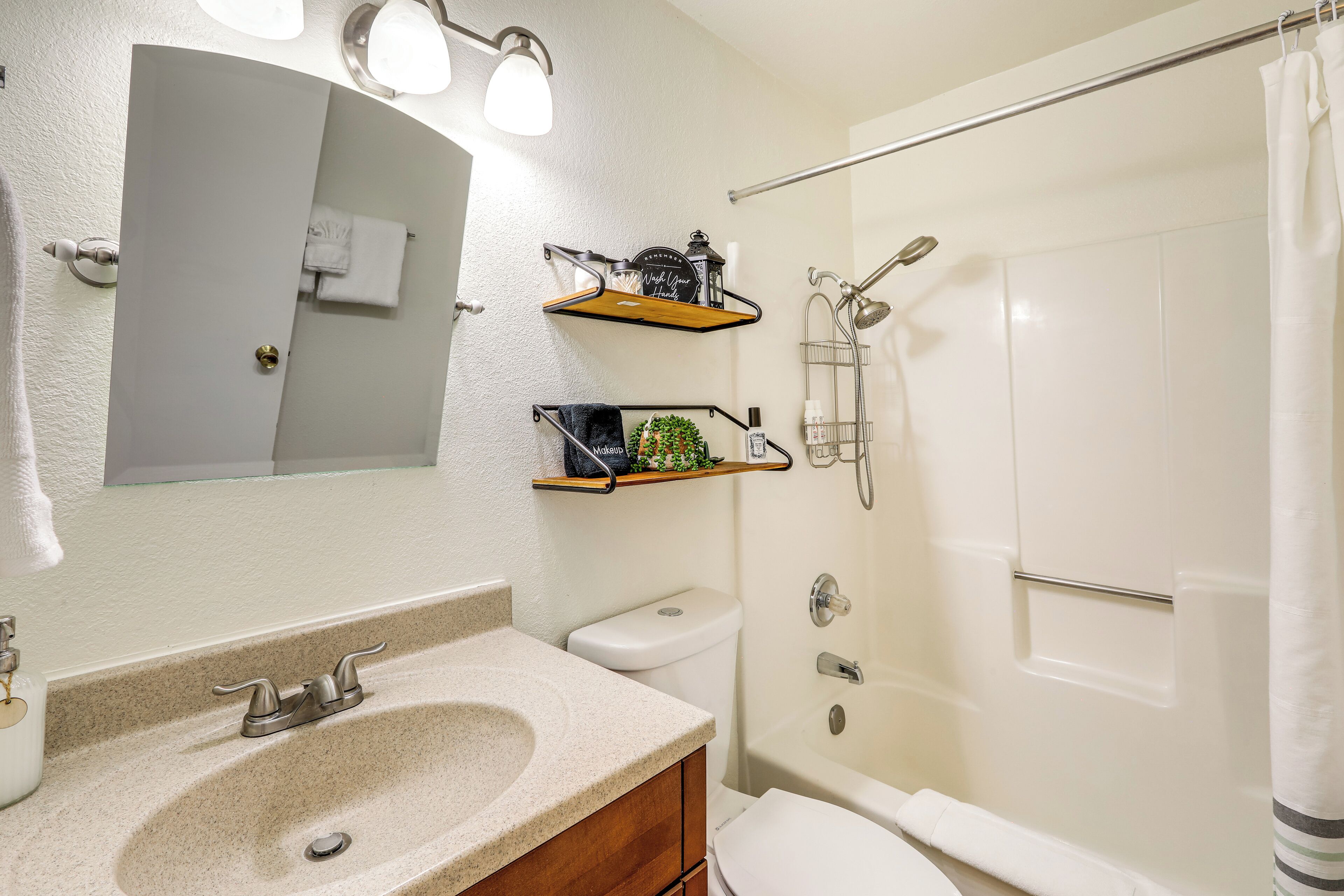 A bathroom with a sink, toilet, and shower. There are shelves above the sink and a towel rack on the wall.