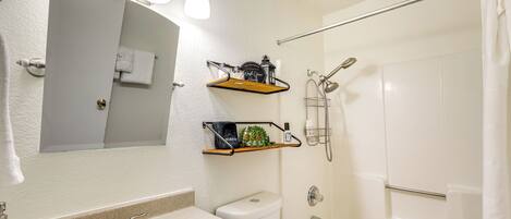 A bathroom with a sink, toilet, and shower. There are shelves above the sink and a towel rack on the wall.
