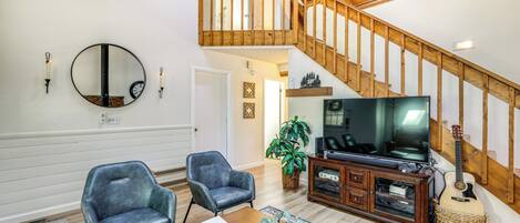 A spacious living room with a wooden staircase, a large TV, and two leather chairs.