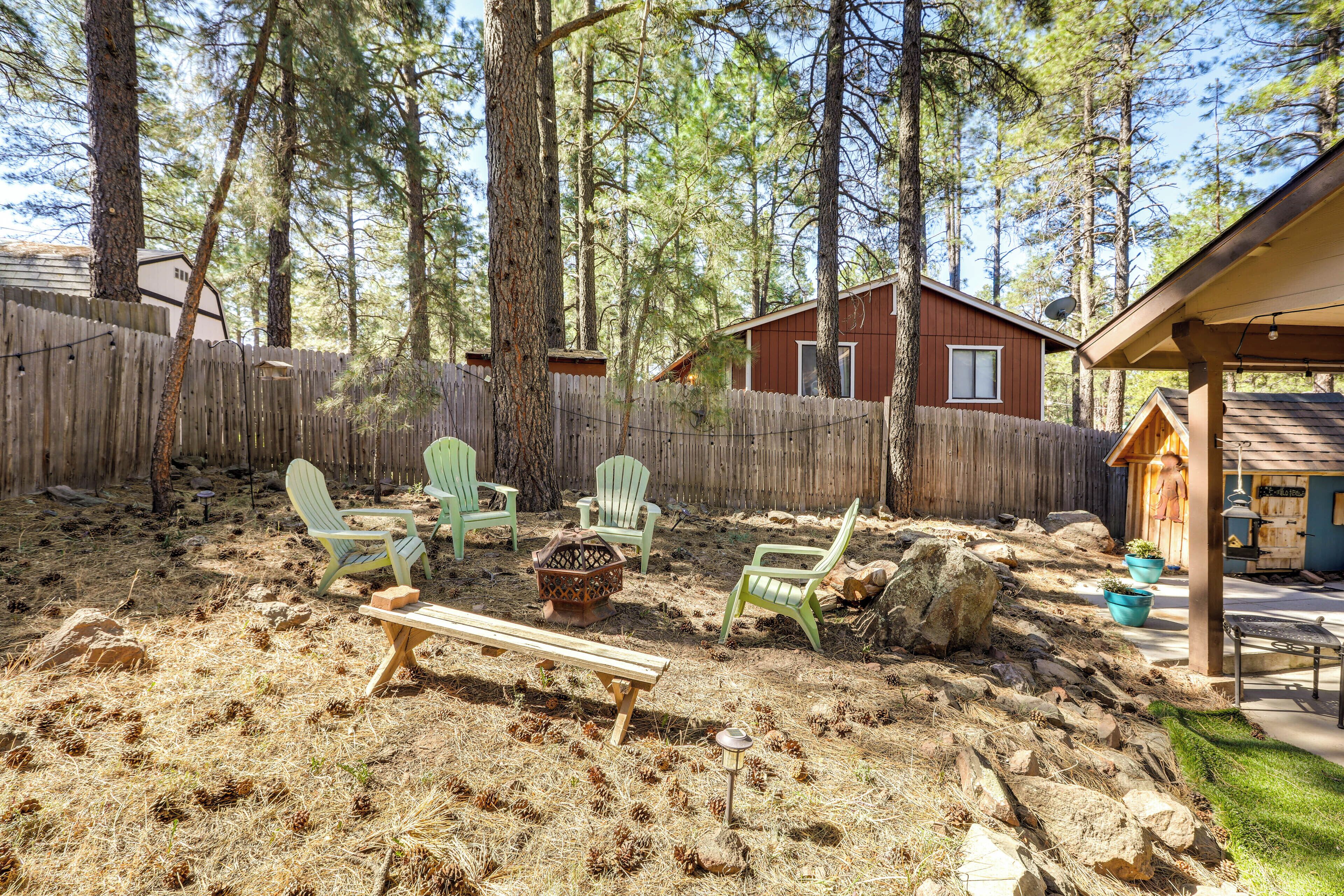 Een achtertuin met een houten terras, groene Adirondack-stoelen, een vuurkuil en een houten bank.