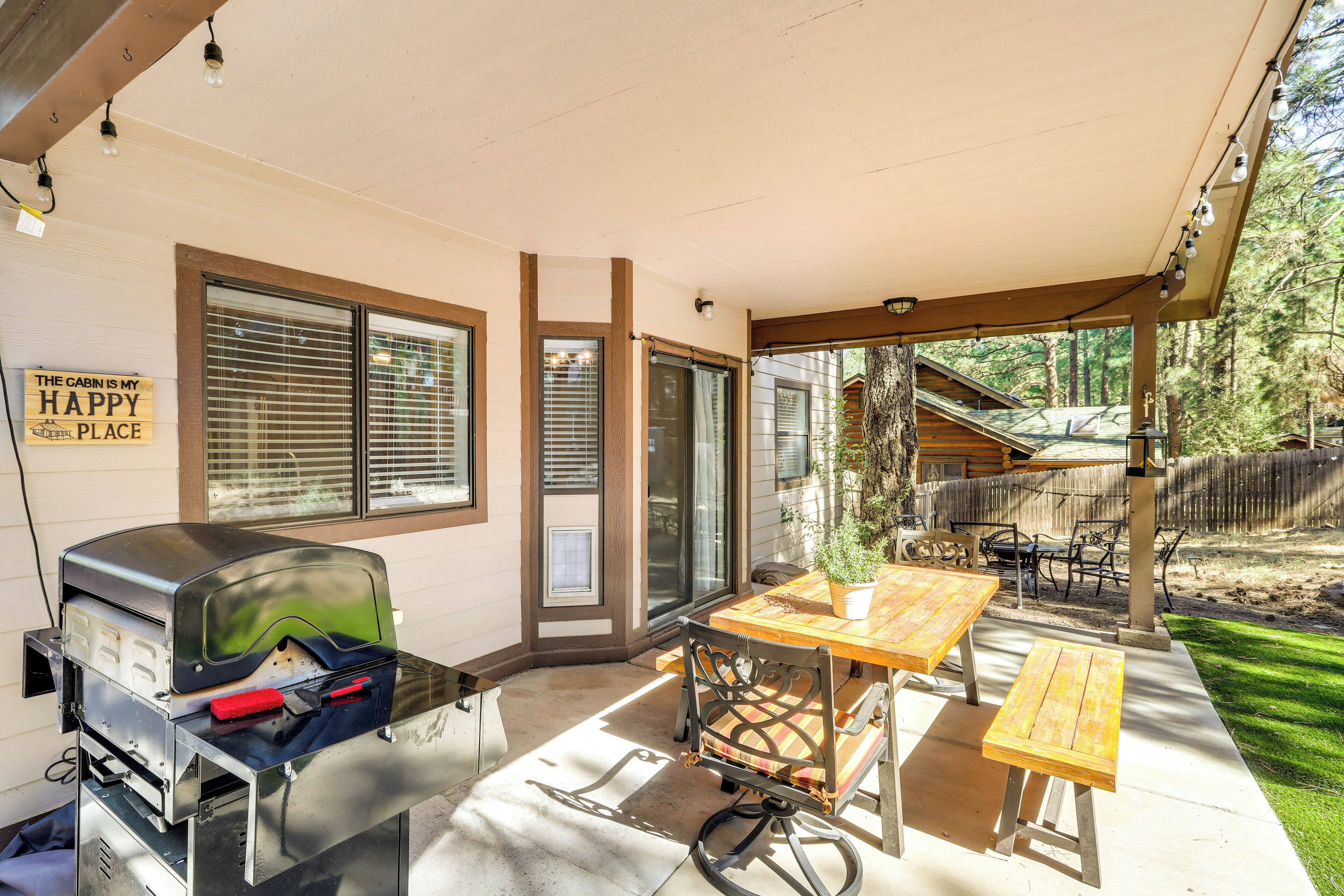 A covered patio with a grill, wooden table, and chairs.